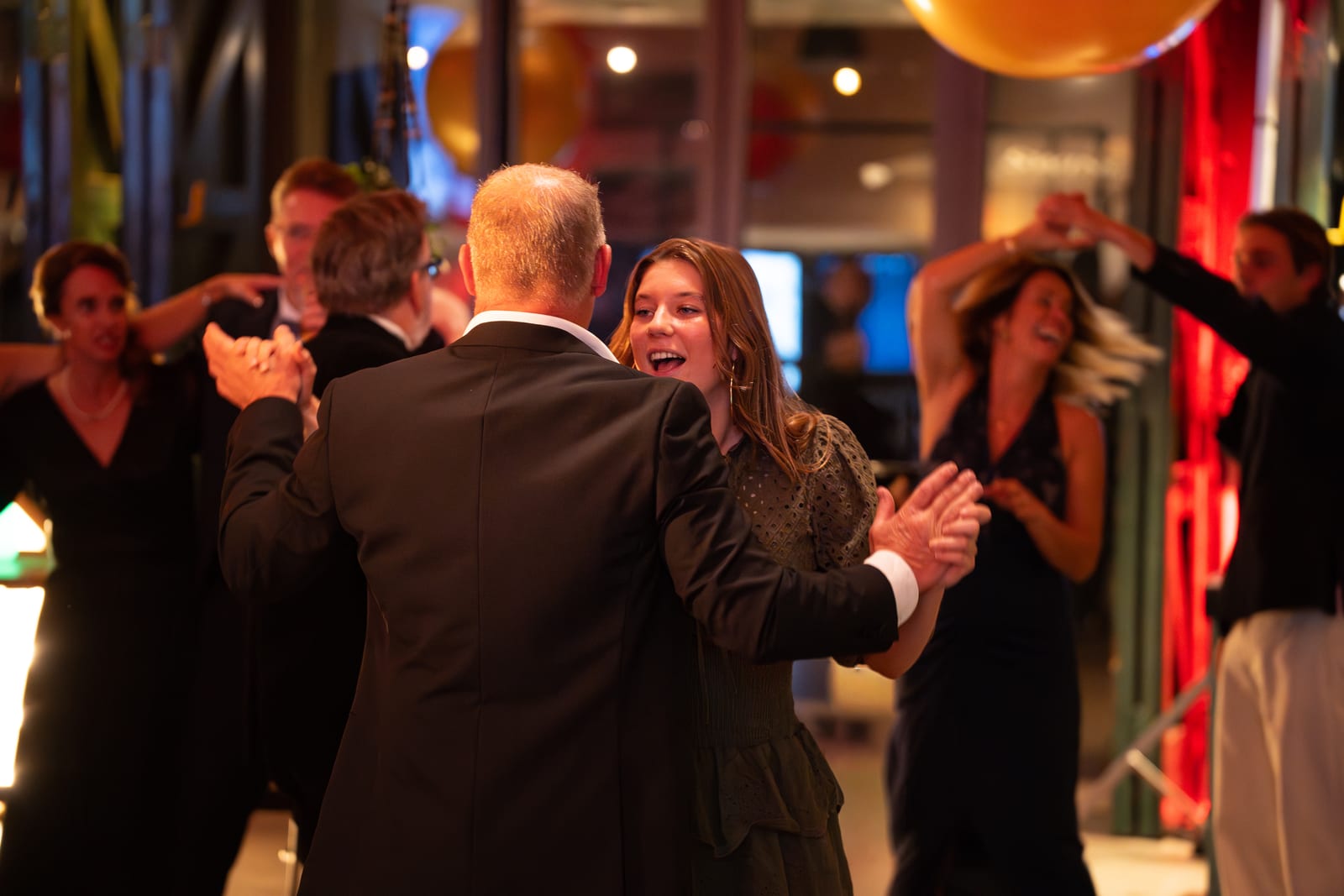 Dansende paren op de dansvloer, een man en vrouw in het midden lachen naar elkaar terwijl anderen om hen heen bewegen