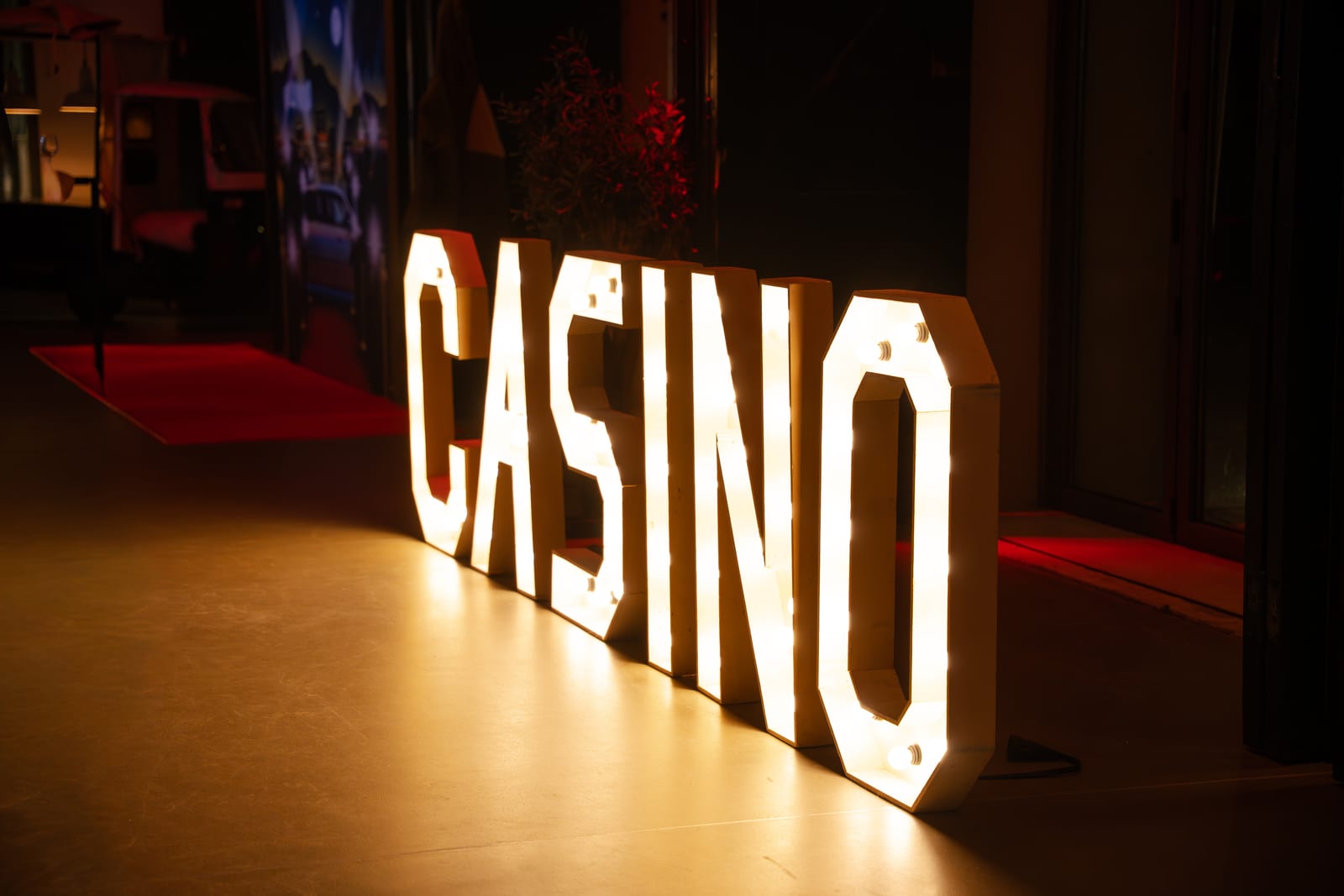Grote verlichte letters die het woord CASINO vormen, opgesteld op de vloer bij de ingang met een rode loper op de achtergrond