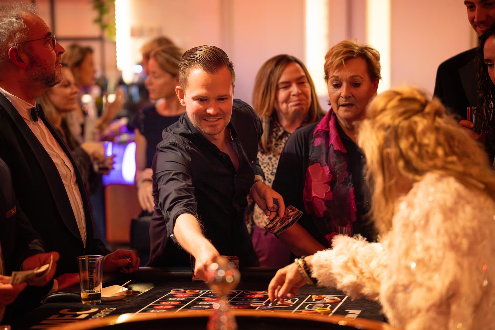 Lachende gasten rond de roulettetafel terwijl een man in het midden zijn fiches op het kleed plaatst