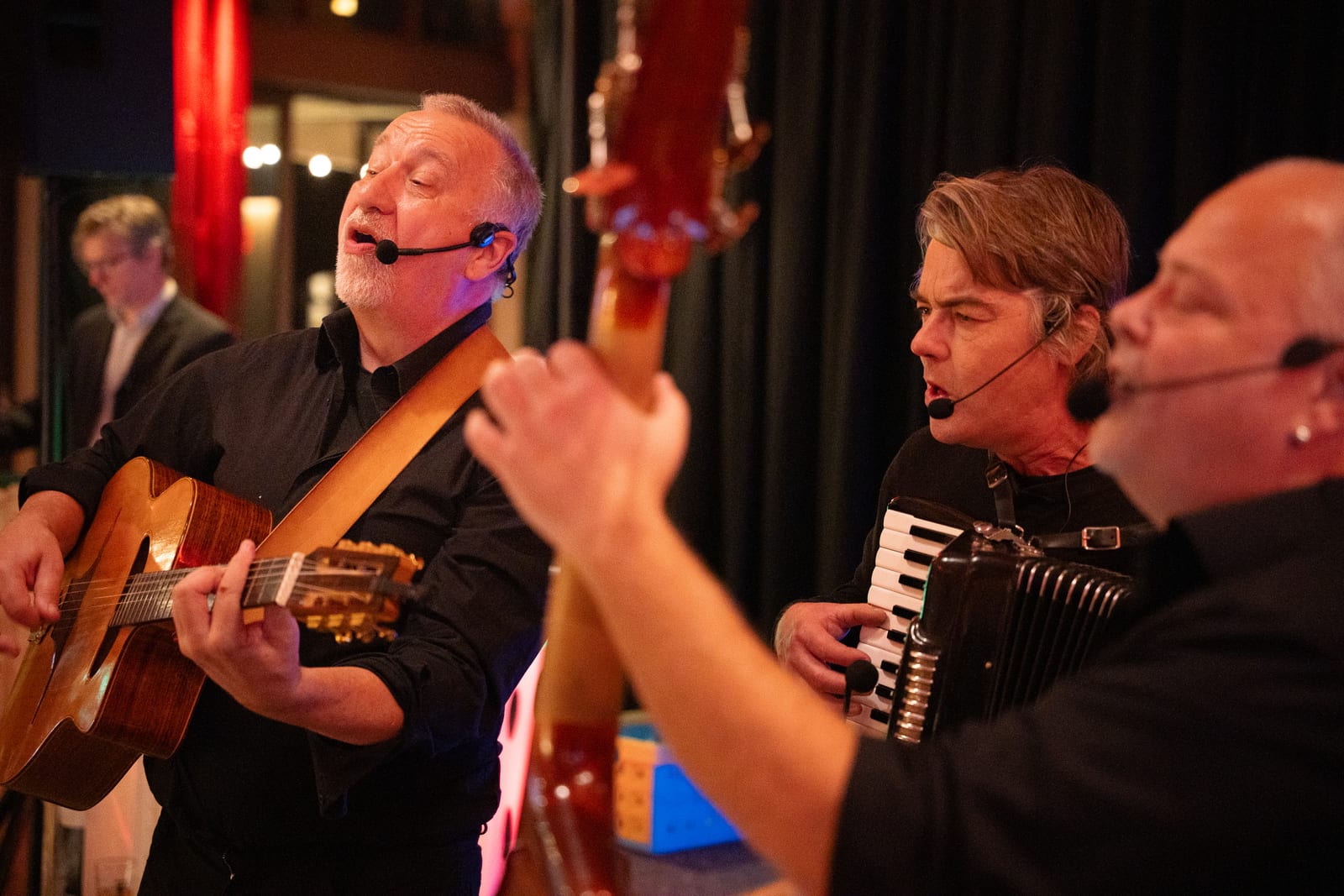 Drie muzikanten van de liveband zingen met headsetmicrofoons terwijl ze gitaar, contrabas en accordeon spelen